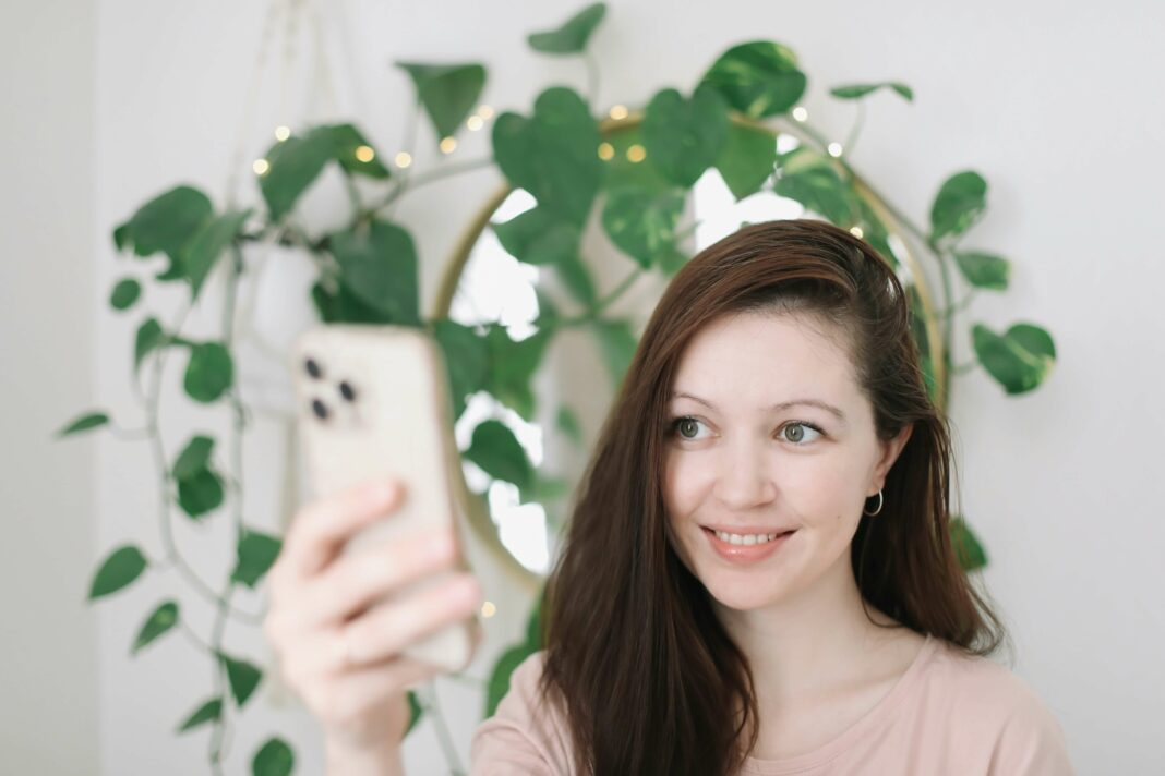 Woman using phone mirror and green plant in background