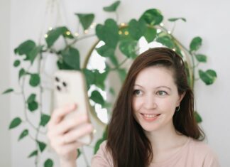 What Are the Environmental Benefits of VoIP? Woman using phone mirror and green plant in background