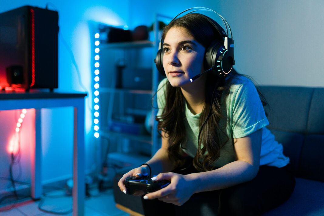 Girl sitting on a couch gaming with headphones on her head surrounded by blue lights