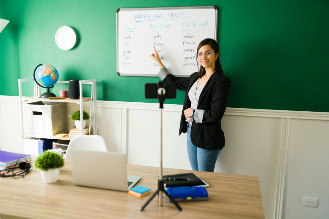 A woman in front of a whiteboard giving a virtual class streaming it through her phone.