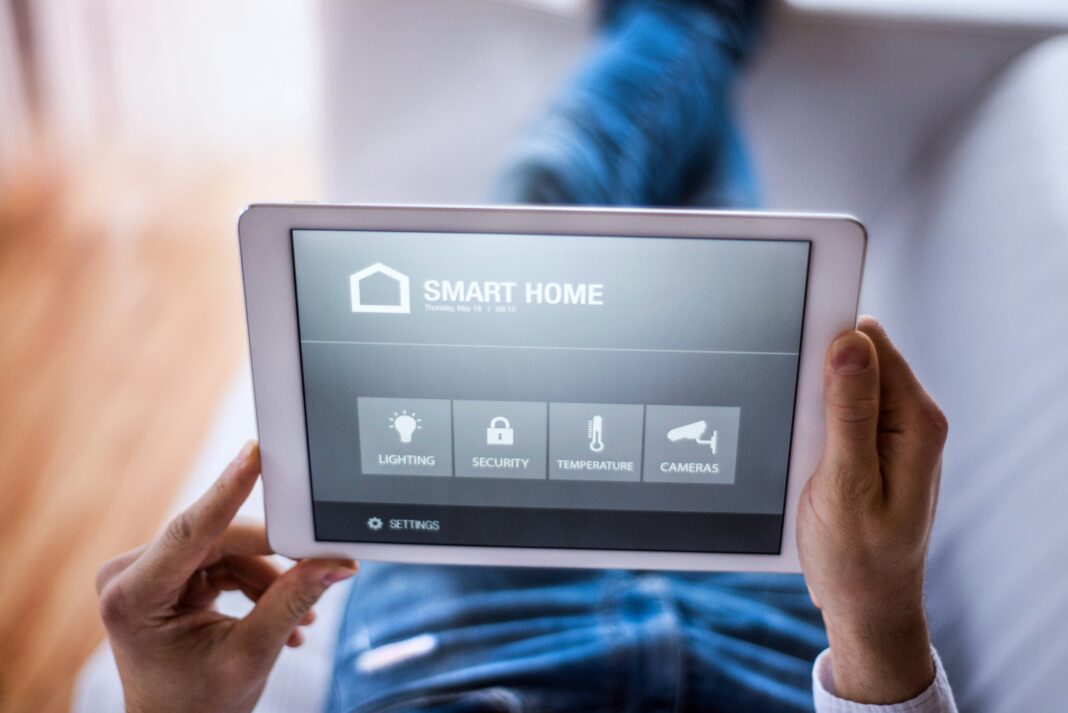 Unrecognisable hand holding a tablet with a smart home app opened on it.