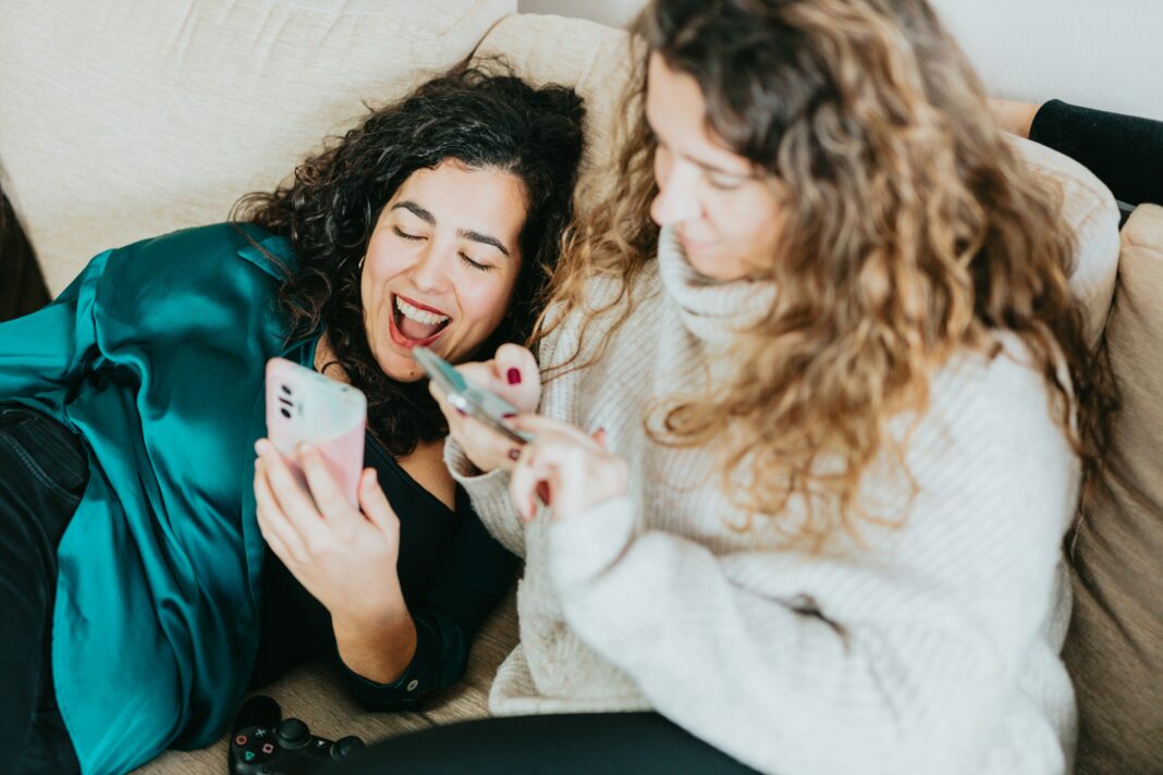 Two friends sitting on a couch laughing while scrolling through social media
