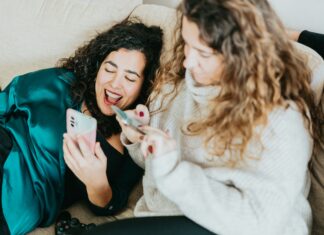 How Does VoIP Integration with Social Media Platforms Enhance Customer Engagement? Two friends sitting on a couch laughing while scrolling through social media