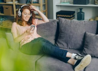 What Role Does Mobile Broadband Play In IoT Connectivity? A woman sitting on her couch smiling at her phone with headphones on.