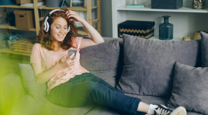 What Role Does Mobile Broadband Play In IoT Connectivity? A woman sitting on her couch smiling at her phone with headphones on.