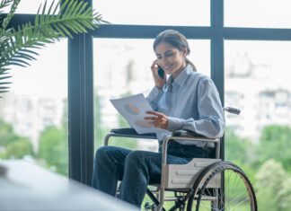 Can Connectivity Improve Accessibility for Persons with Disabilities? Photo of a woman sitting in a wheel chair, smiling and talking on the phone while looking at a piece of paper