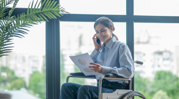 Can Connectivity Improve Accessibility for Persons with Disabilities? Photo of a woman sitting in a wheel chair, smiling and talking on the phone while looking at a piece of paper