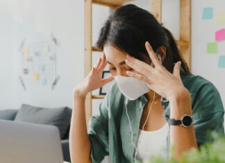 Can VoIP Really Transform Your Business Operations? Woman sitting at her desk in front of her laptop with a mask on