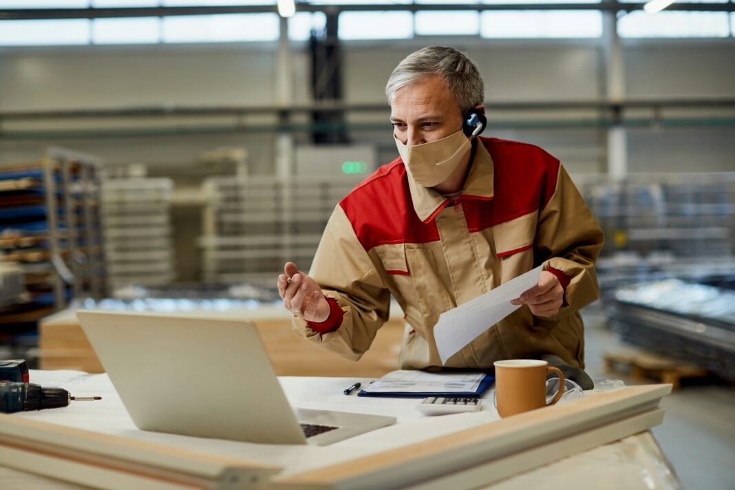 Man sitting at his desk with his computer and a mask on face having a meeting