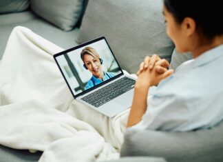 How to Set Up VoIP for Your Business in 5 Easy Steps Woman sitting on her couch under a white blaket video calling someone on her laptop