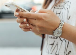 5G vs Full Fibre: What’s the Difference? A person wearing a watching standing while typing on their phone