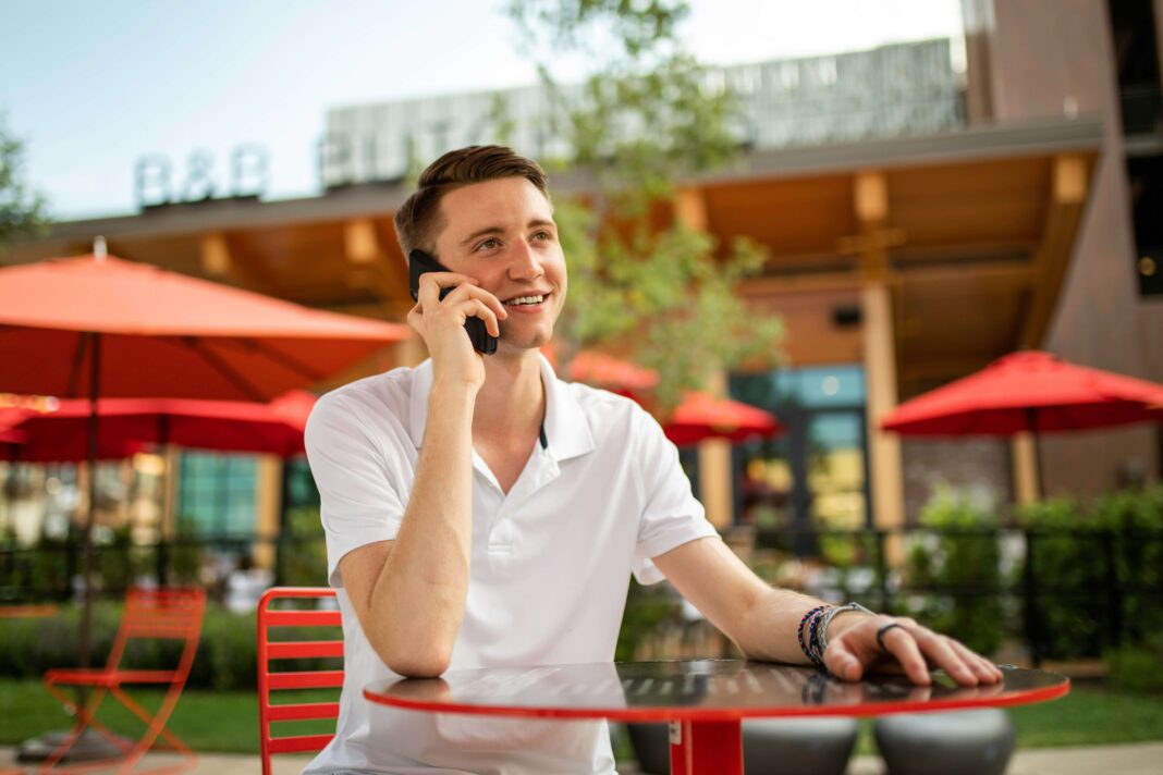 A man sitting outside a shop at a table talking on his phone