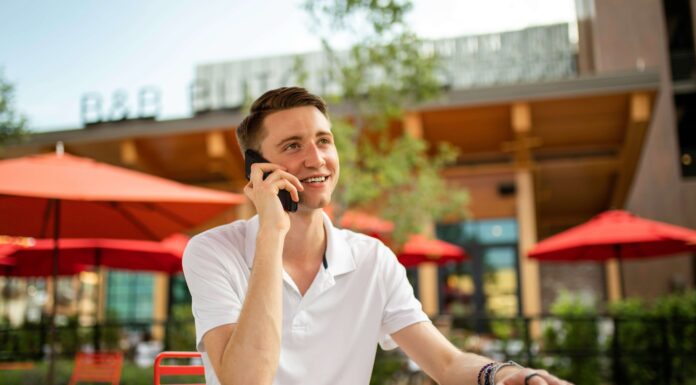 Are VoIP Phones Expensive? A man sitting outside a shop at a table talking on his phone