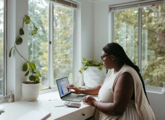 Is Full Fibre Environmentally Friendly? A woman sitting at her desk surrounded by windows and plants working on her laptop