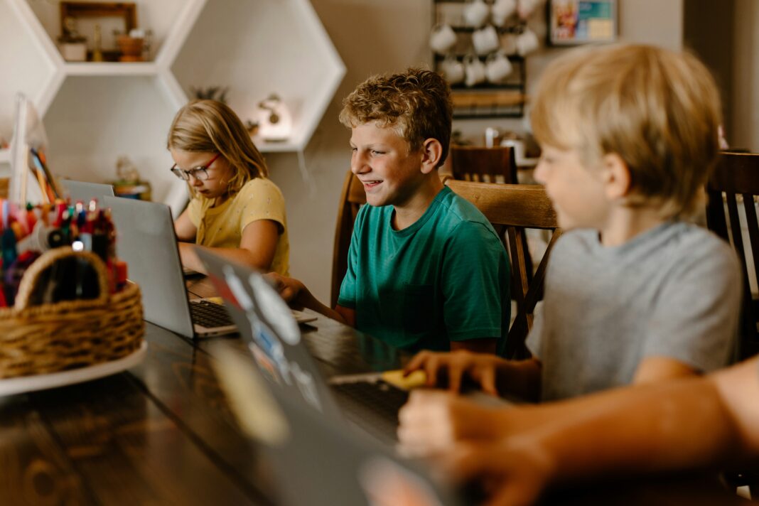 What Are the Economic Benefits of Broadband Investment? Three children sitting at a table with their laptops doing work