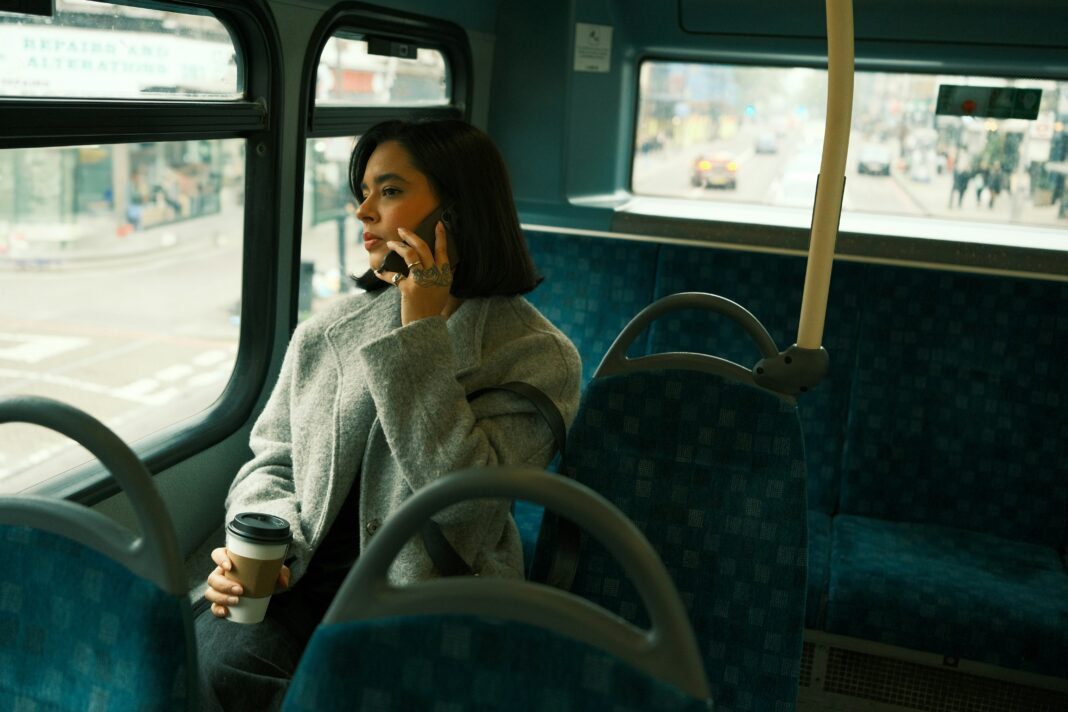 A woman wearing a jacket sitting on a bus while talking on the phone