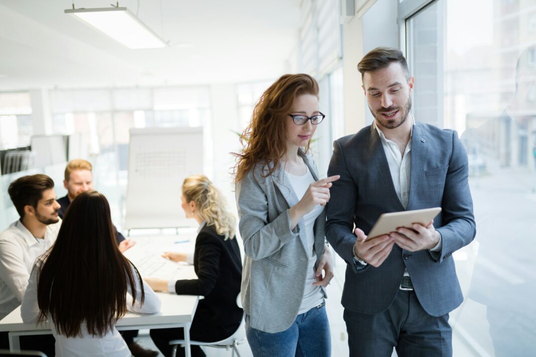 A man and a woman standing in an office and talking while looking at a tablet