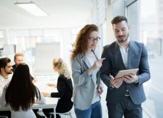 7 Factors That Affect Business Broadband Speed A man and a woman standing in an office and talking while looking at a tablet