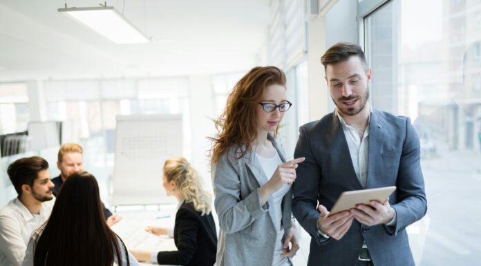 7 Factors That Affect Business Broadband Speed A man and a woman standing in an office and talking while looking at a tablet