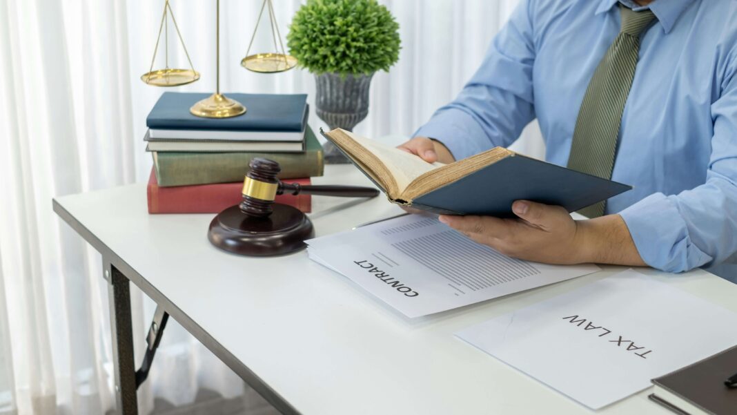 A man reading a book while sitting at his desk with a gavel laying next to him