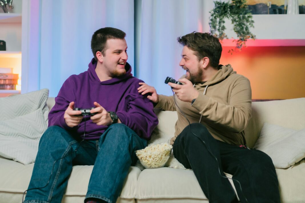 Two men sitting on a couch with gaming remotes laughing