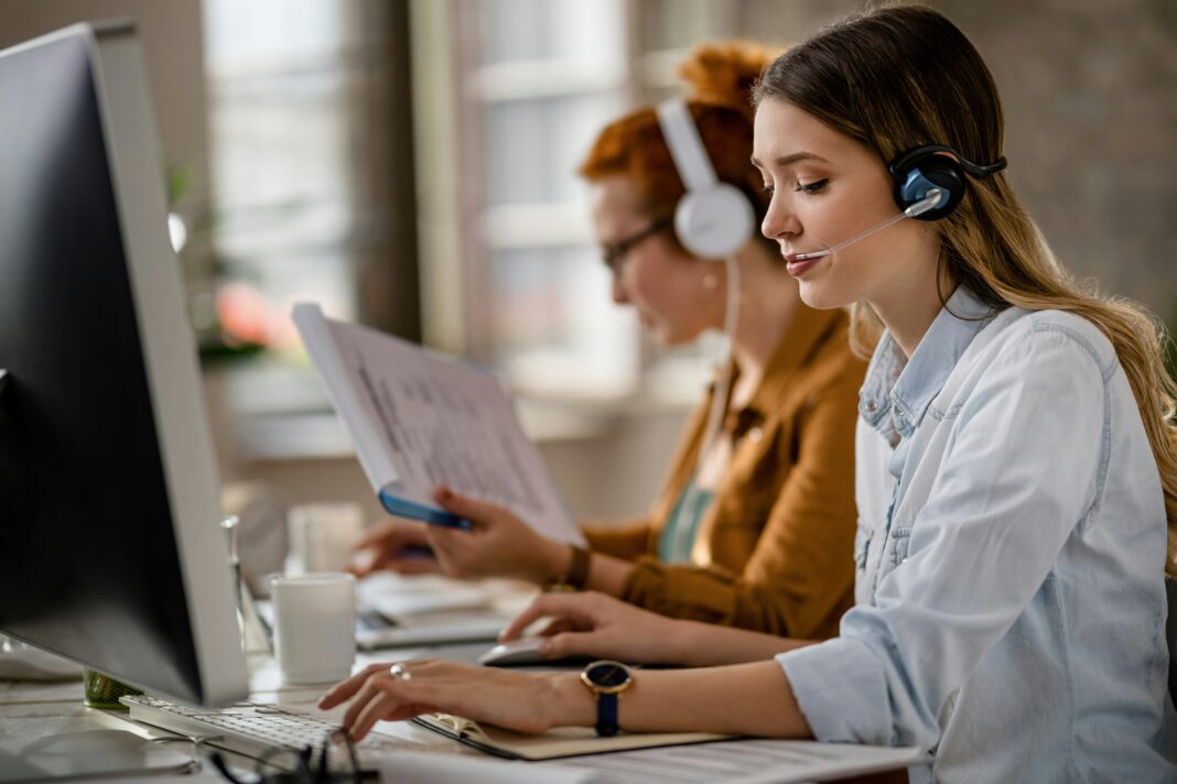 A woman sitting at her desk in front of a computer screen with a headset on