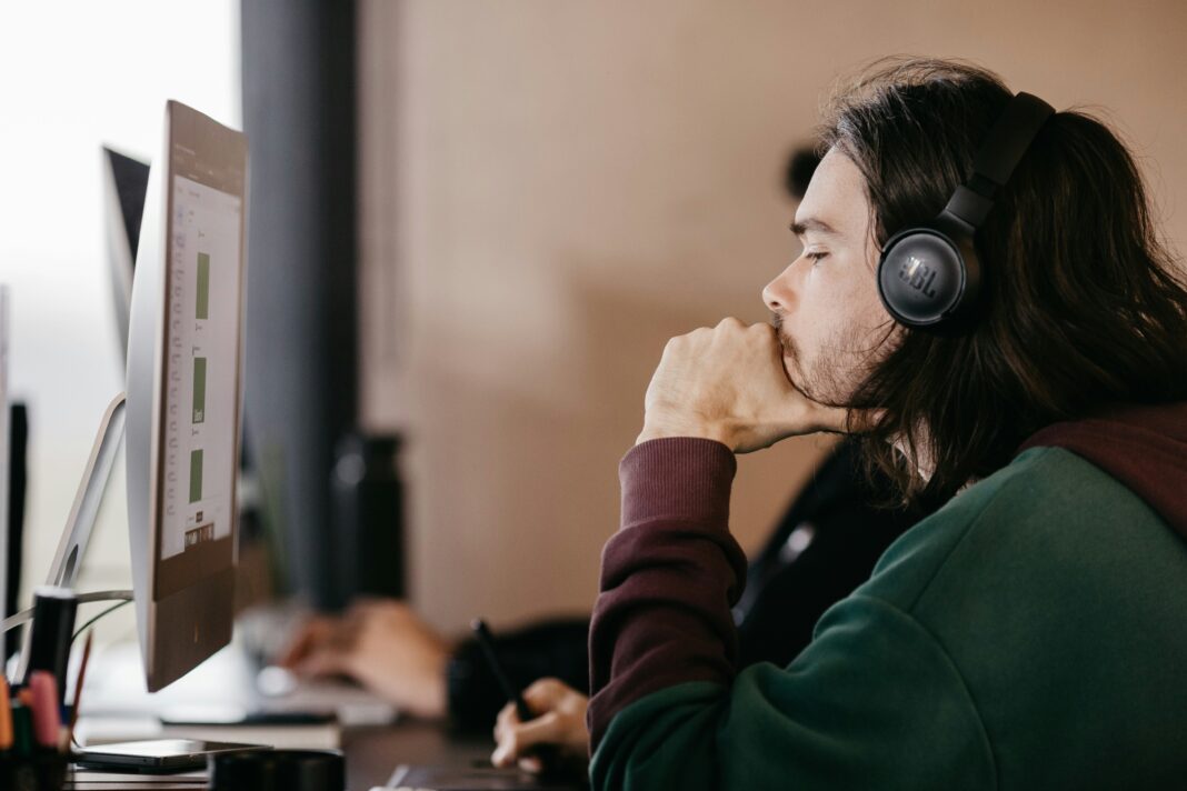 A man sitting at a desk looking at a computer screen with a headset on