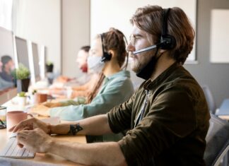 How Can I Test VoIP Call Quality? A man sitting at his desk next to a woman looking at a computer screen while wearing a headset
