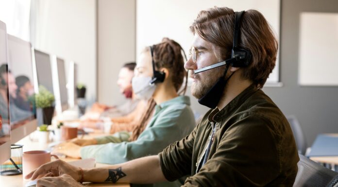 How Can I Test VoIP Call Quality? A man sitting at his desk next to a woman looking at a computer screen while wearing a headset