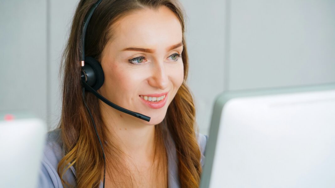 A woman sitting in front of her computer screen with a headset on