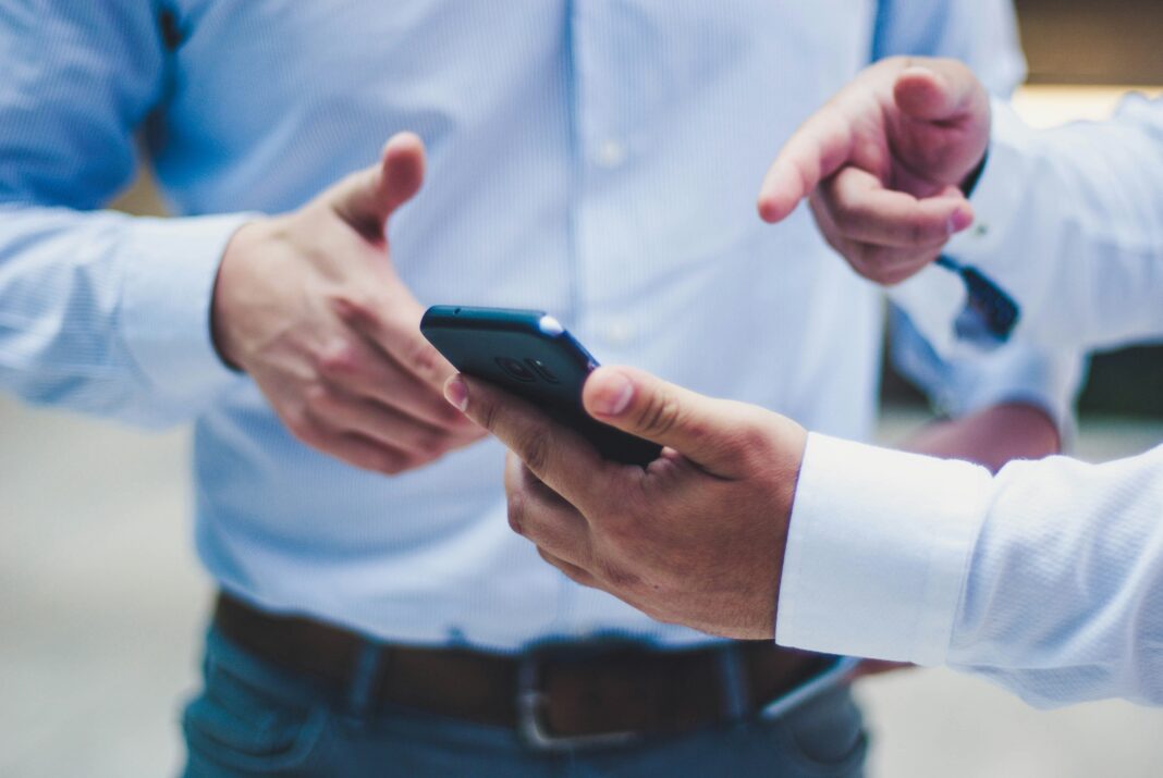 Using Mobile Data as Broadband A man standing with a phone in his hand pointing at it while talking to another man