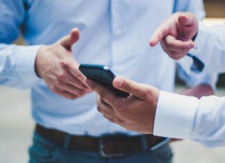 Using Mobile Data as Broadband A man standing with a phone in his hand pointing at it while talking to another man