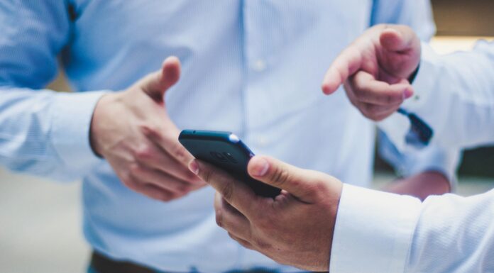 Using Mobile Data as Broadband A man standing with a phone in his hand pointing at it while talking to another man