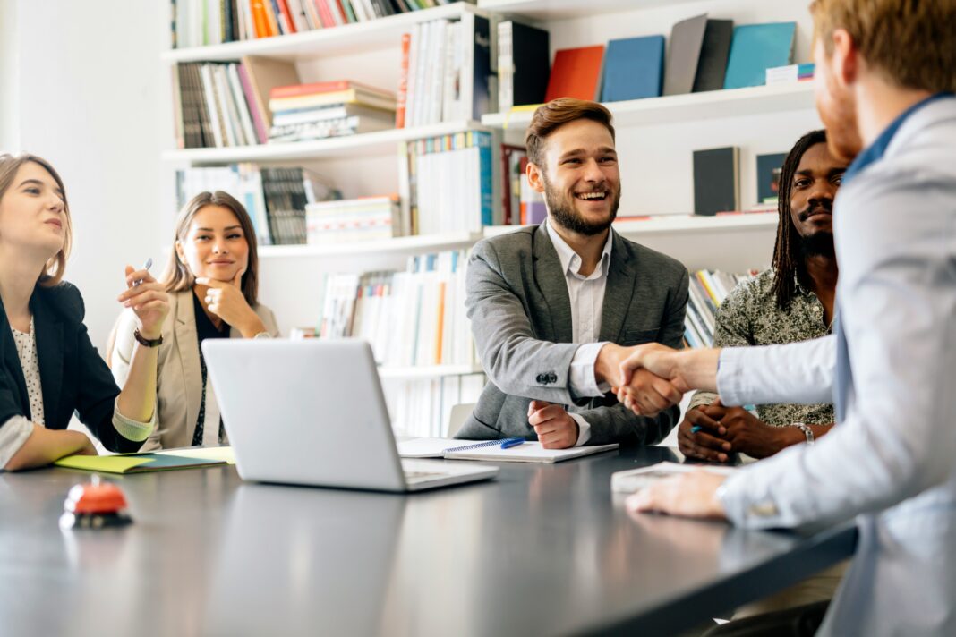 A group of people sitting around an office table smiling and shaking hands