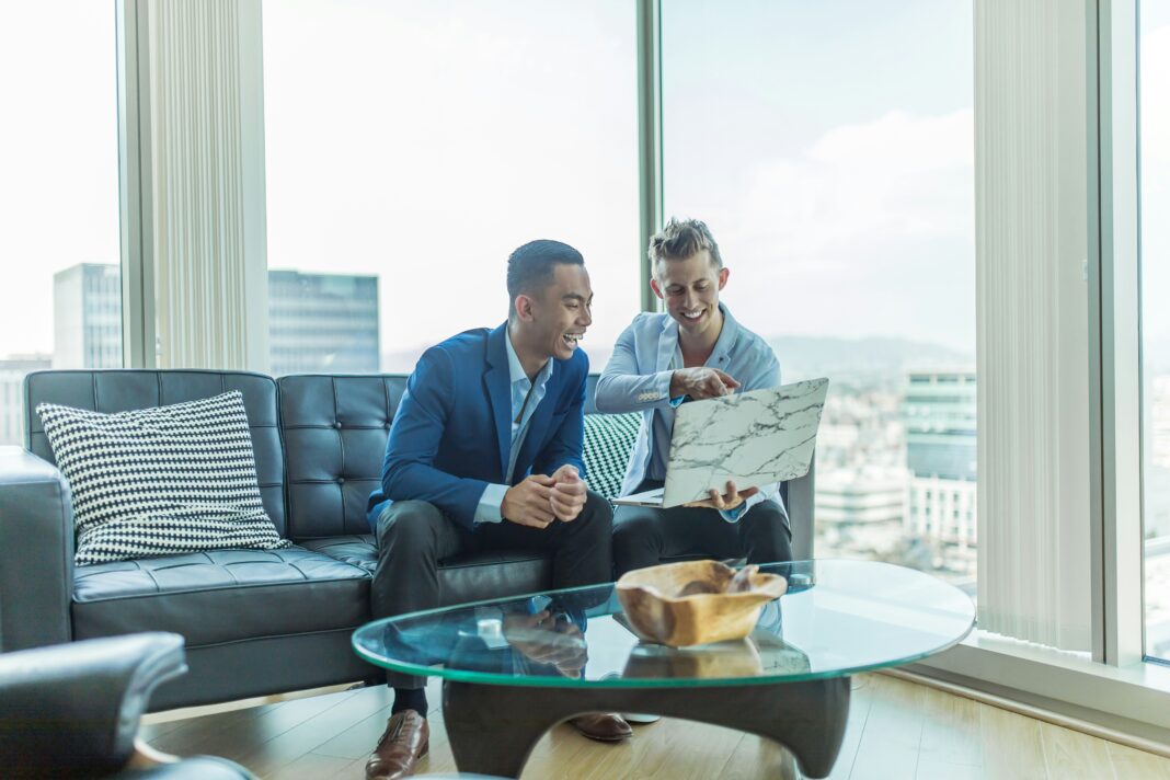 Two men sitting in an office talking while looking at a laptop