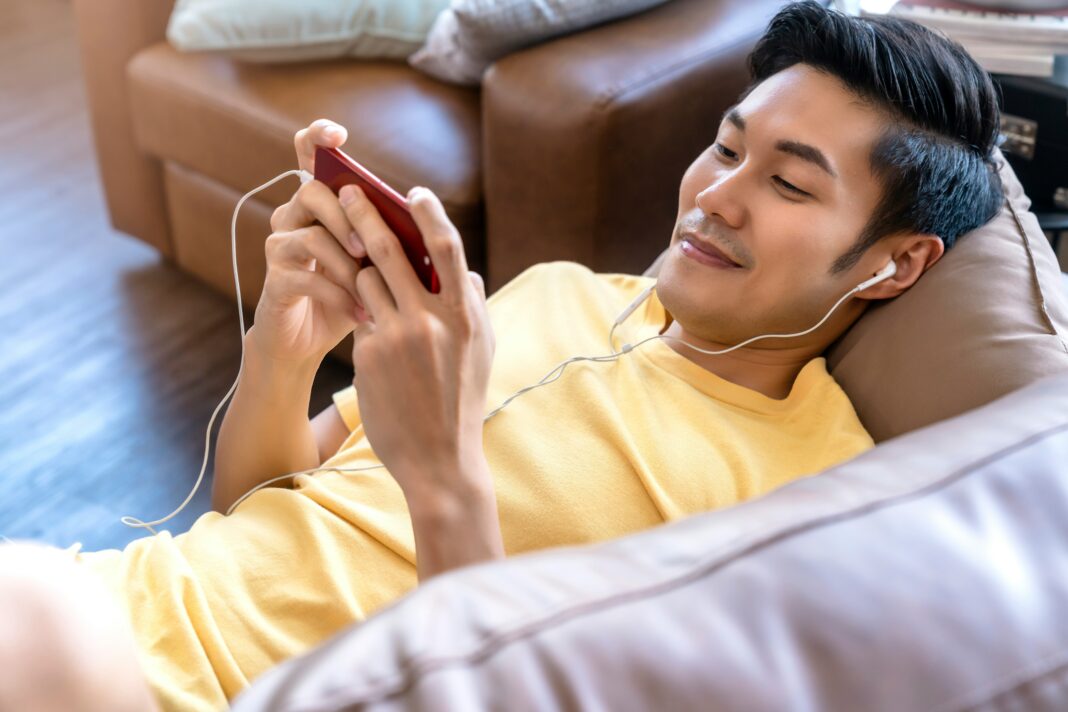 A man laying on a couch with earphones in watching a video on his phone