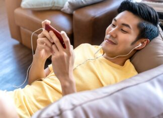 Best UK Mobile Network Coverage in 2025 A man laying on a couch with earphones in watching a video on his phone