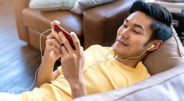 Best UK Mobile Network Coverage in 2025 A man laying on a couch with earphones in watching a video on his phone