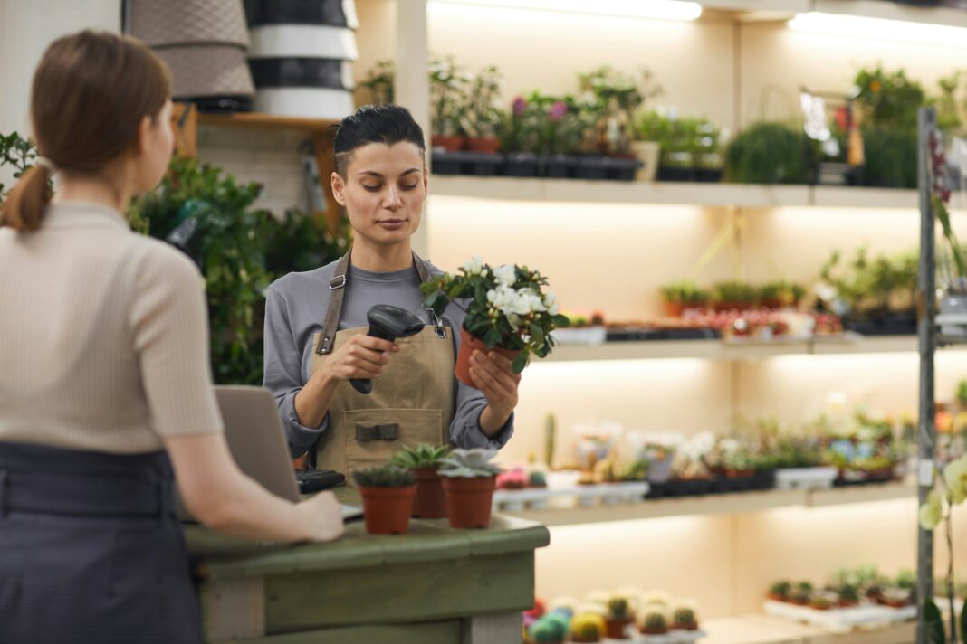 A woman behind a counter in a nursery helping a customer while holding a plant