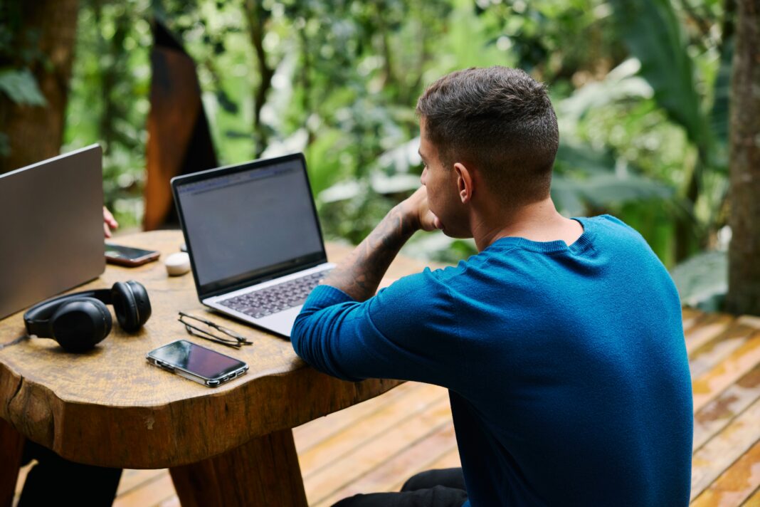A man sitting at a wooden table outside working on his laptop
