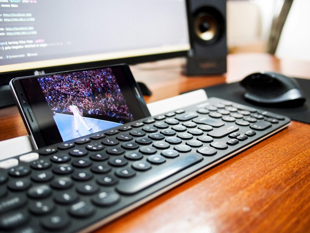 A photo of a phone resting behind a keyboard streaming a video