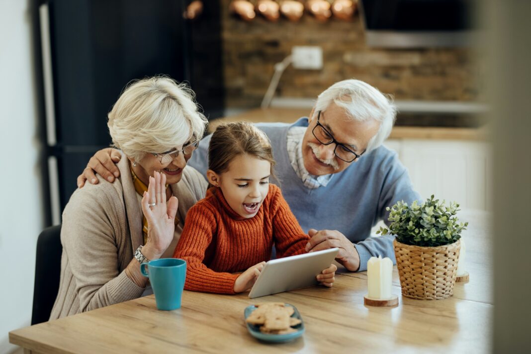 Grandparents and their grandson sitting at a table with coffee video calling on a tablet