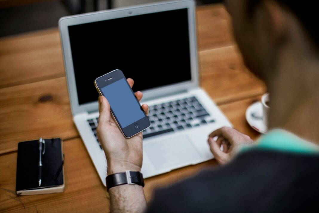 A man sitting at a wooden table with his laptop and phone