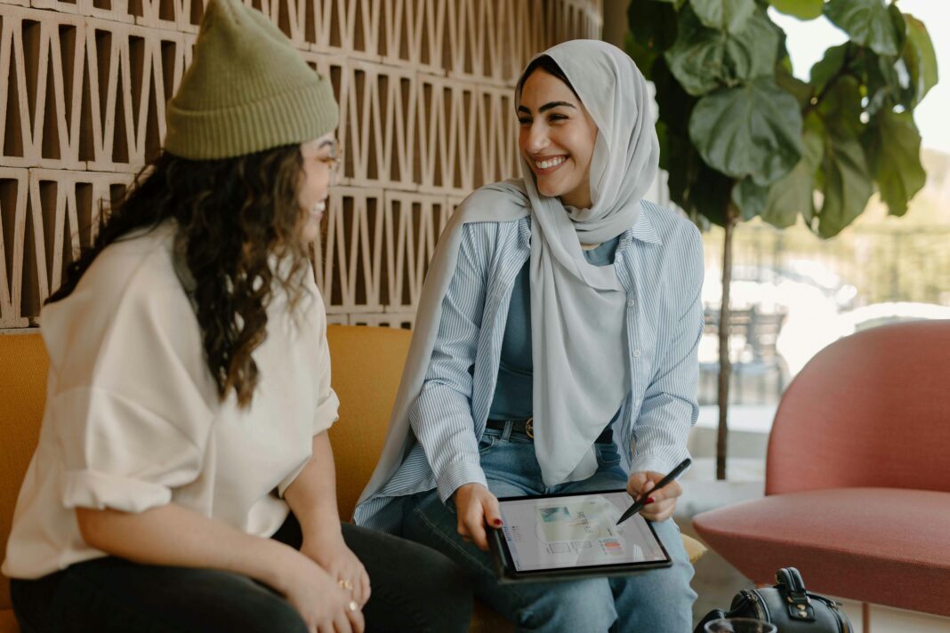 Two women sitting on a couch in an office with a tablet