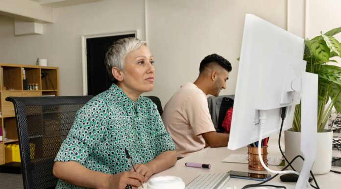 What is The Fastest Internet Speed in the UK? A woman sitting at her desk looking at her computer screen while writing in a notebook