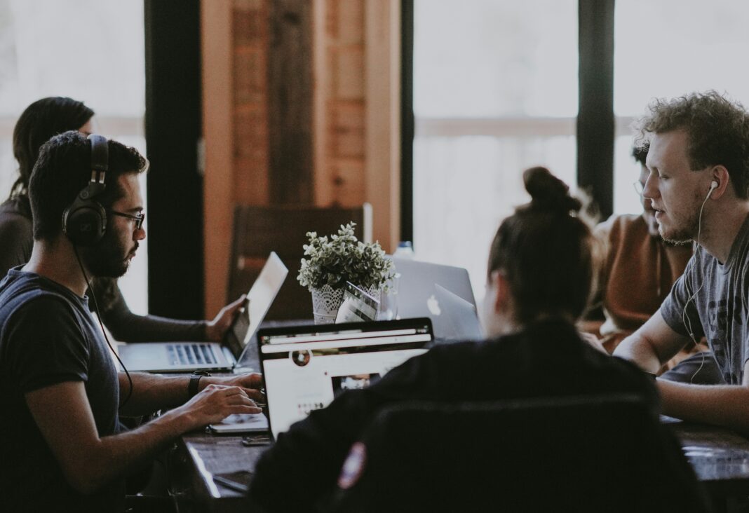 Why VoIP Should Be Part of Your Company’s Digital Communication Policy people-working-shared-co-working-desk-with-quality-headsets