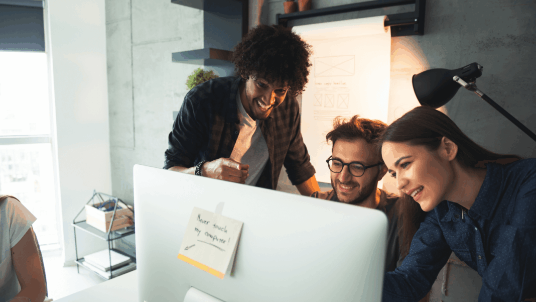 startup-employees-around-computer-screen-smiling